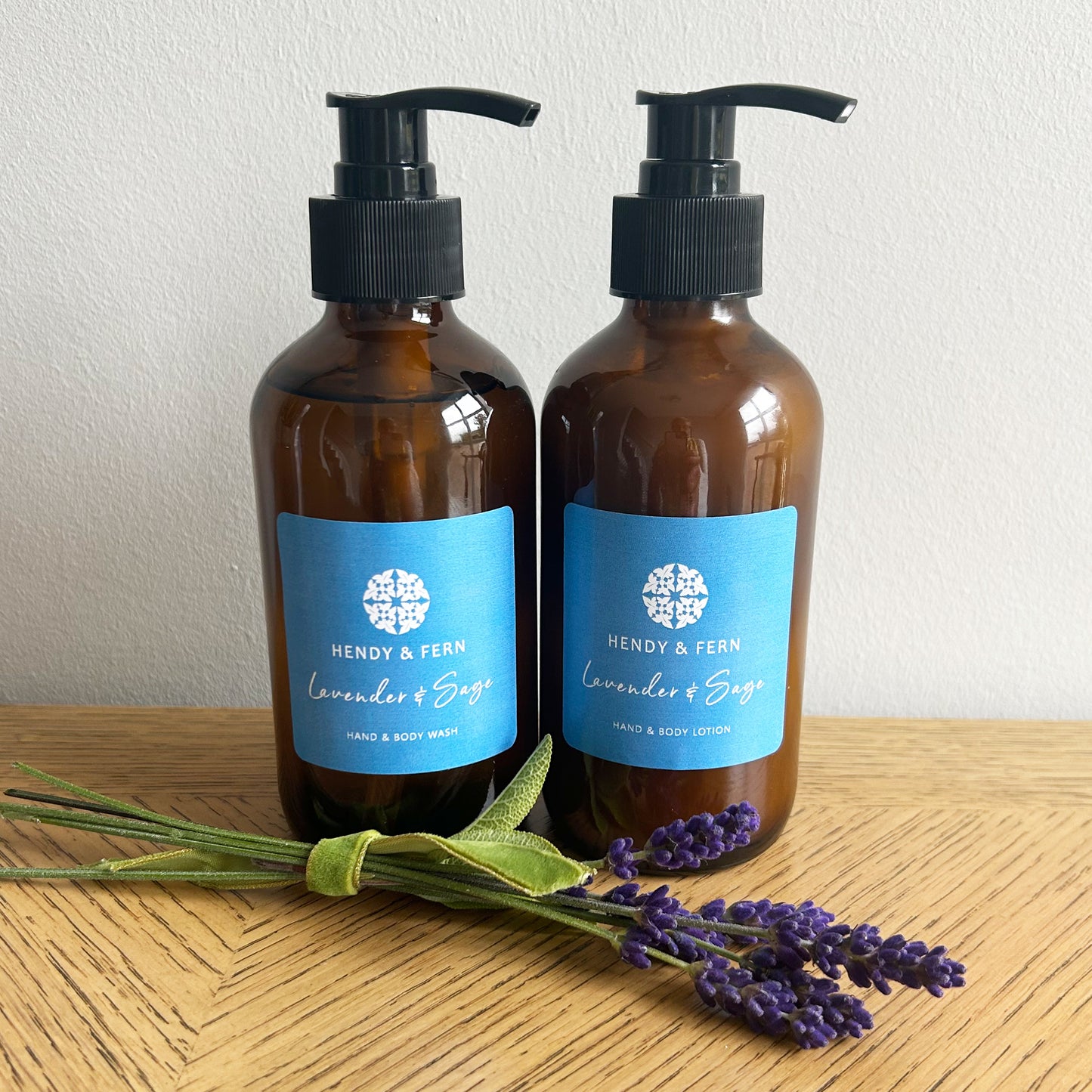 Liquid hand soap and lotion set - lavender and clary sage bottles on a wooden surface next to a sprig of lavender