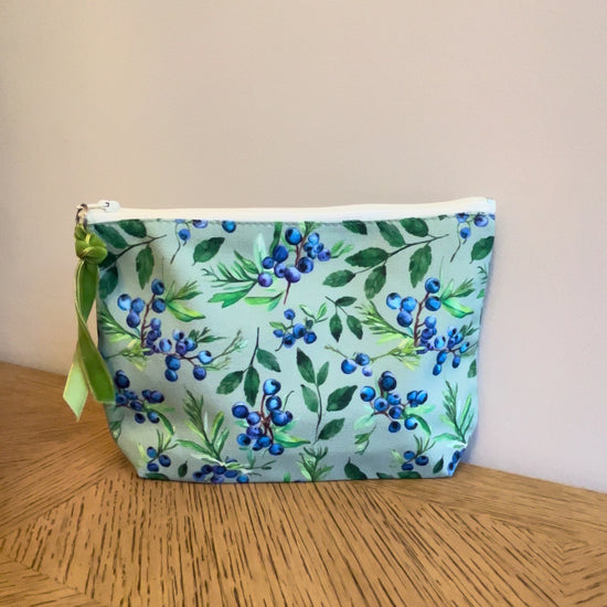 Green cosmetic toiletry bag with a juniper berry and mint print lined with a zip and gusset. Labelled Made in the UK.