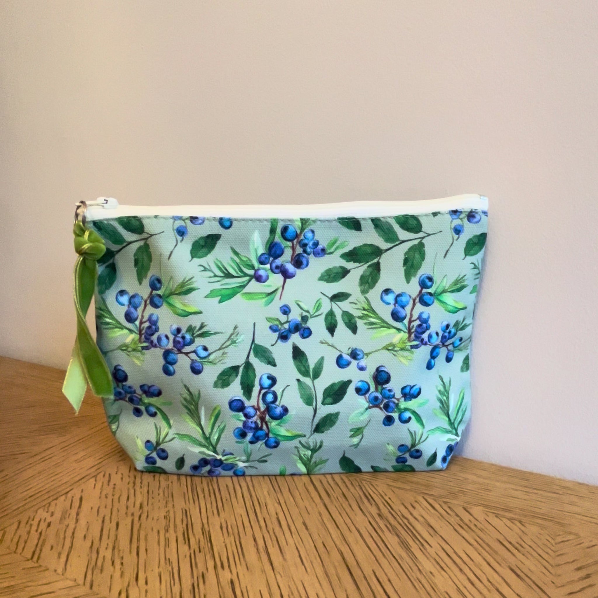 Green cosmetic toiletry bag with a juniper berry and mint print lined with a zip and gusset. Labelled Made in the UK.